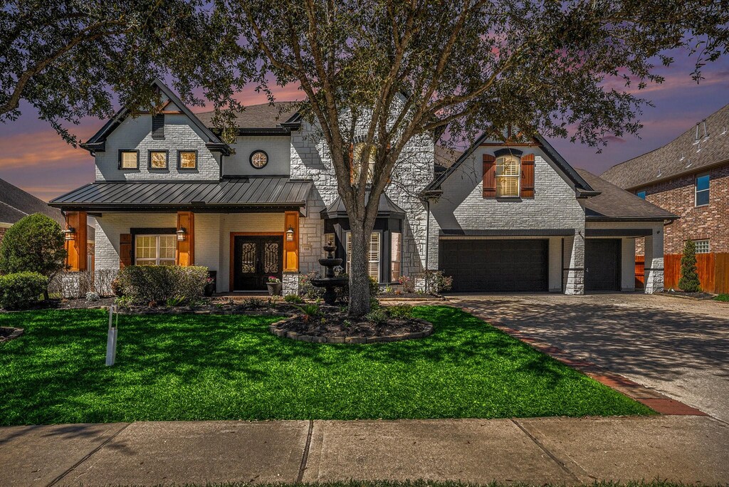 3318 King George Ln, Friendswood, TX 77546 - view of front of house featuring a front yard, a standing seam roof, concrete driveway, stone siding, and metal roof