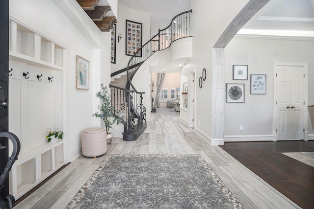 foyer with stairway, arched walkways, baseboards, and wood finished floors