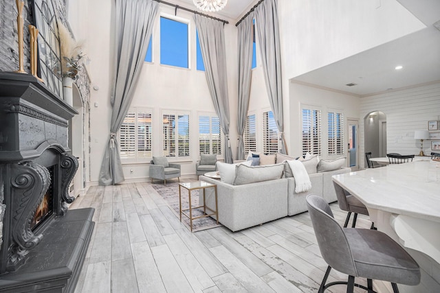 living room featuring crown molding, wood finished floors, a towering ceiling, and a lit fireplace