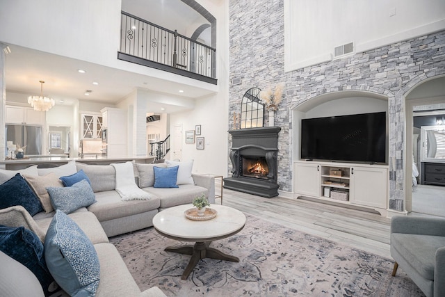 living room with visible vents, a stone fireplace, a high ceiling, an inviting chandelier, and light wood-style floors