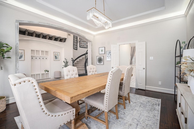 dining space with an inviting chandelier, a tray ceiling, arched walkways, and dark wood-type flooring