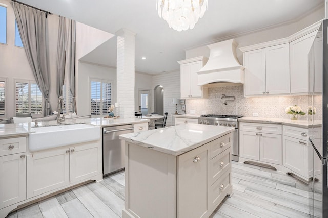 kitchen featuring light stone counters, a sink, custom range hood, appliances with stainless steel finishes, and backsplash