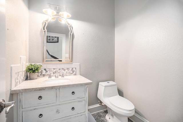 bathroom with vanity, toilet, a textured wall, and baseboards