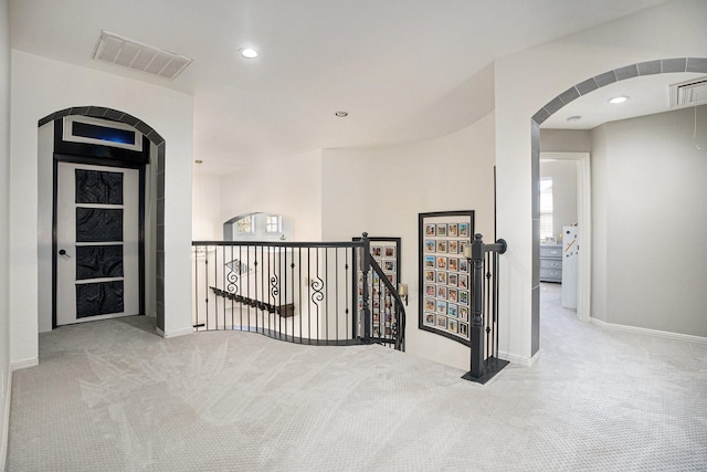 hallway with visible vents, an upstairs landing, and carpet