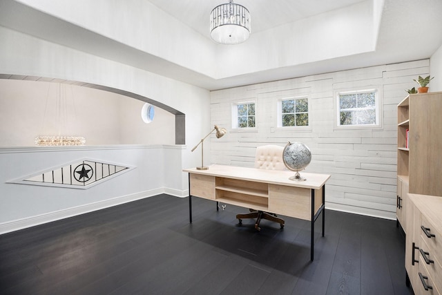 home office with baseboards, dark wood-style flooring, arched walkways, a raised ceiling, and a notable chandelier