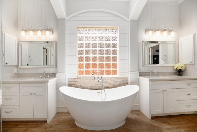 bathroom featuring a freestanding bath, two vanities, wood finished floors, and a sink