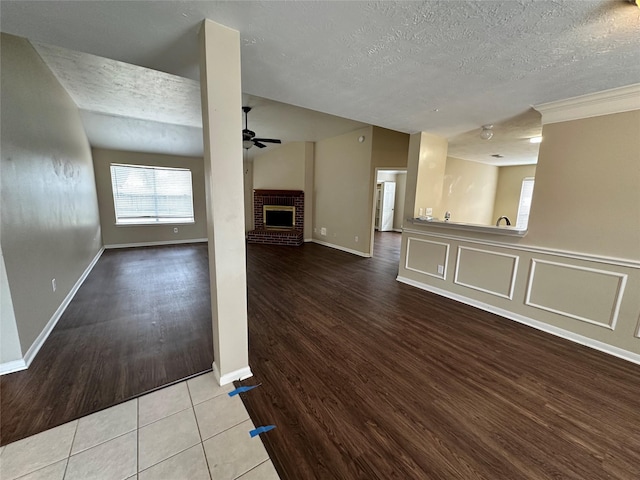 unfurnished living room with a fireplace, a textured ceiling, a ceiling fan, and wood finished floors