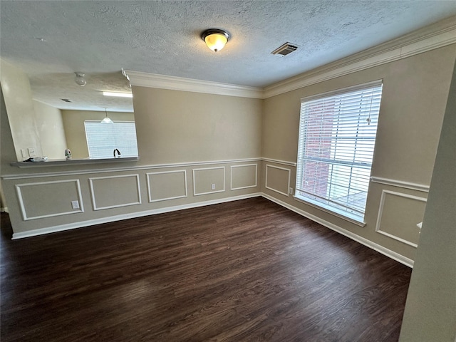 spare room with dark wood-style floors, visible vents, a textured ceiling, crown molding, and a decorative wall