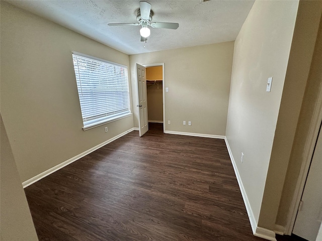 unfurnished bedroom featuring baseboards, ceiling fan, dark wood-type flooring, a textured ceiling, and a walk in closet