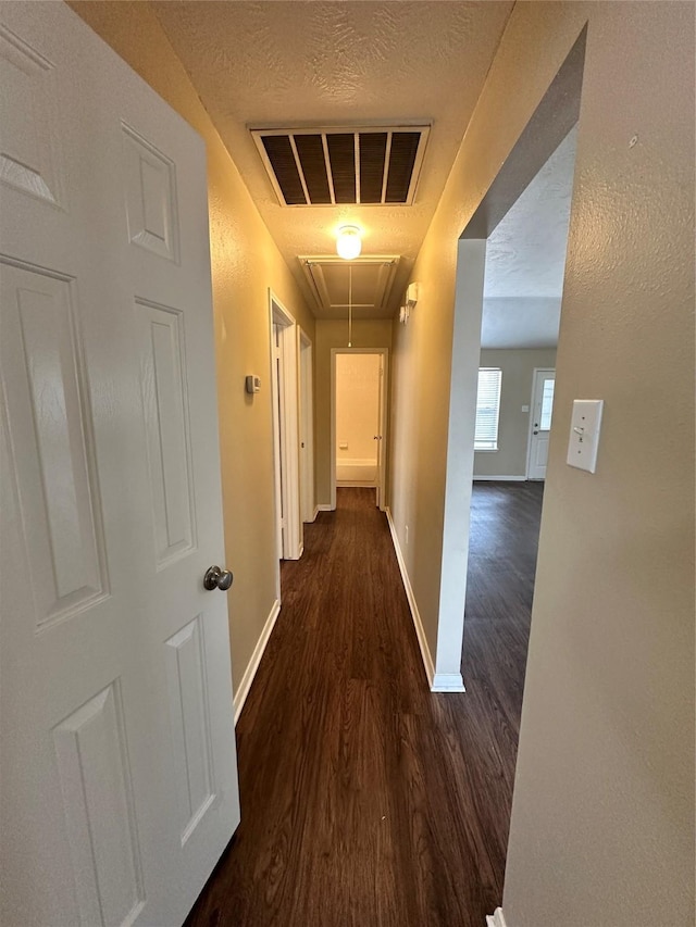 hallway with visible vents, a textured ceiling, wood finished floors, baseboards, and attic access