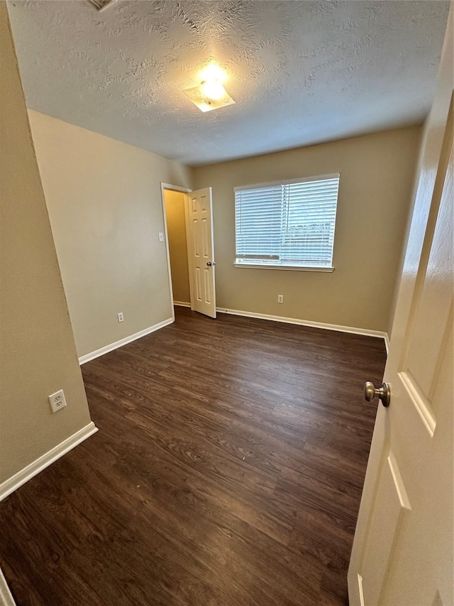 unfurnished bedroom featuring baseboards, dark wood-style flooring, and a textured ceiling