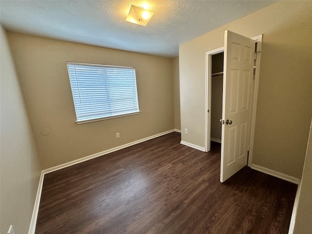 unfurnished bedroom featuring dark wood-type flooring, baseboards, a closet, and a textured ceiling