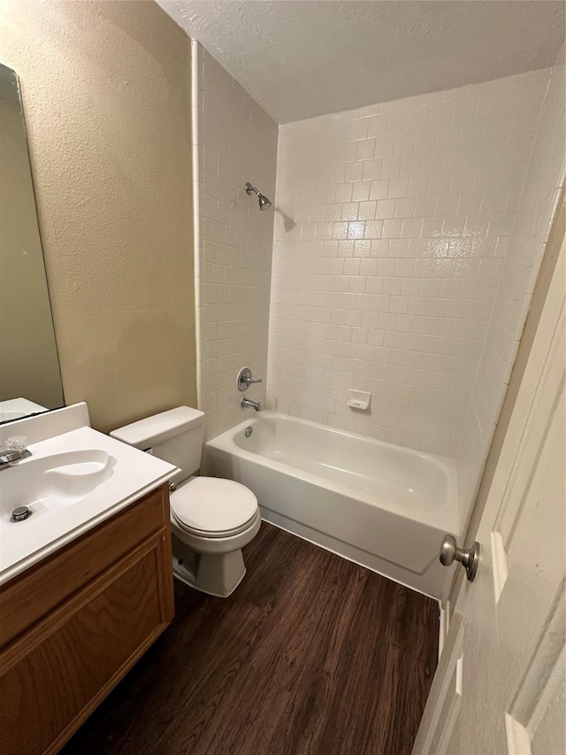 bathroom with toilet, vanity, wood finished floors, a textured ceiling, and washtub / shower combination