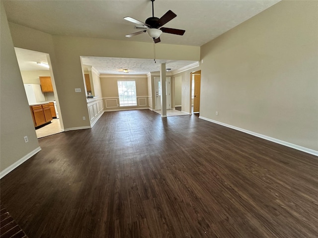 unfurnished living room featuring dark wood-type flooring, crown molding, baseboards, and ceiling fan