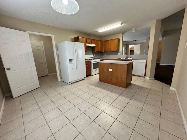 kitchen featuring brown cabinets, a sink, under cabinet range hood, white appliances, and light countertops