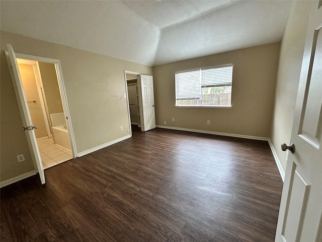 unfurnished bedroom with dark wood finished floors, vaulted ceiling, baseboards, and a textured ceiling