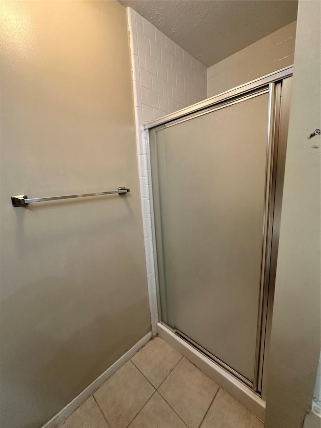 bathroom featuring tile patterned flooring, a shower stall, baseboards, and a textured ceiling