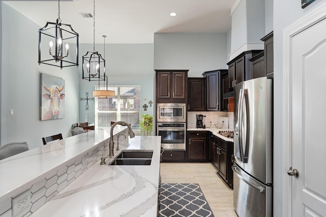 kitchen featuring a sink, appliances with stainless steel finishes, light wood-type flooring, decorative backsplash, and pendant lighting