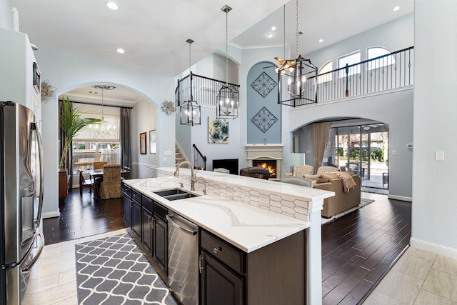 kitchen with a warm lit fireplace, appliances with stainless steel finishes, an inviting chandelier, light wood-style floors, and a sink