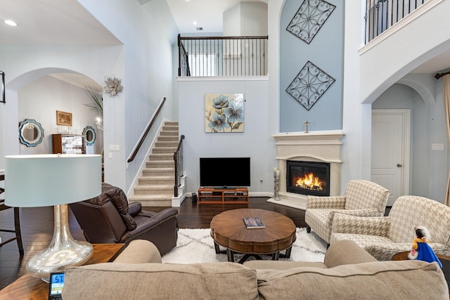 living area featuring arched walkways, a high ceiling, a glass covered fireplace, wood finished floors, and stairs