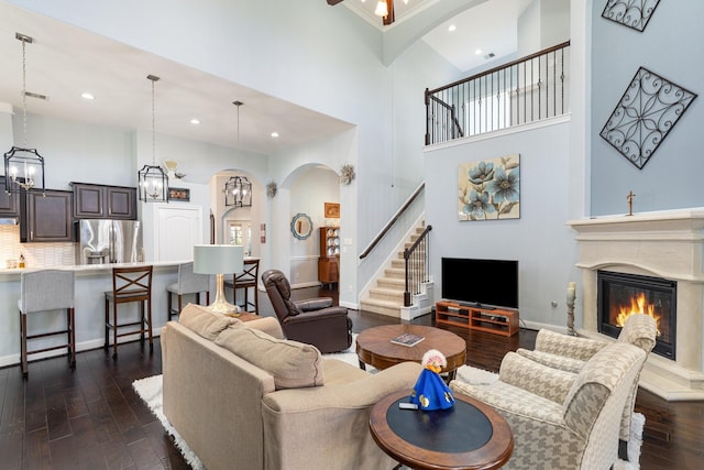 living area with dark wood-style floors, a glass covered fireplace, a towering ceiling, and baseboards