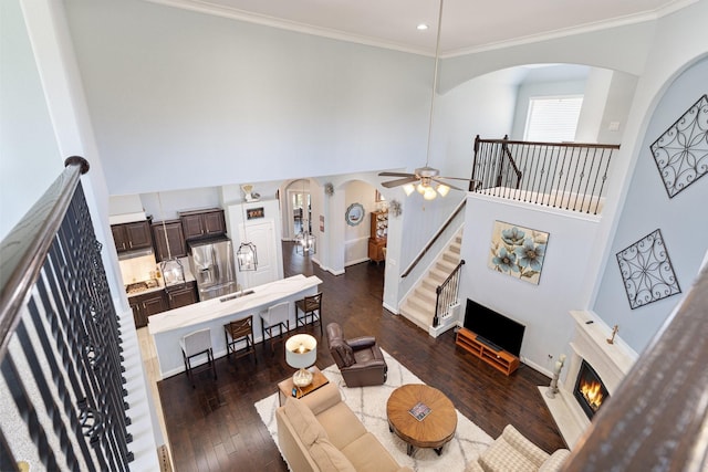 living room with ornamental molding, arched walkways, a warm lit fireplace, and dark wood-style flooring