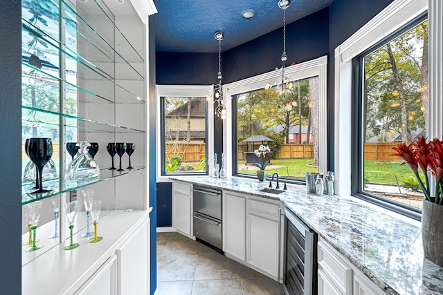 kitchen featuring a textured ceiling, beverage cooler, light stone countertops, white cabinets, and pendant lighting