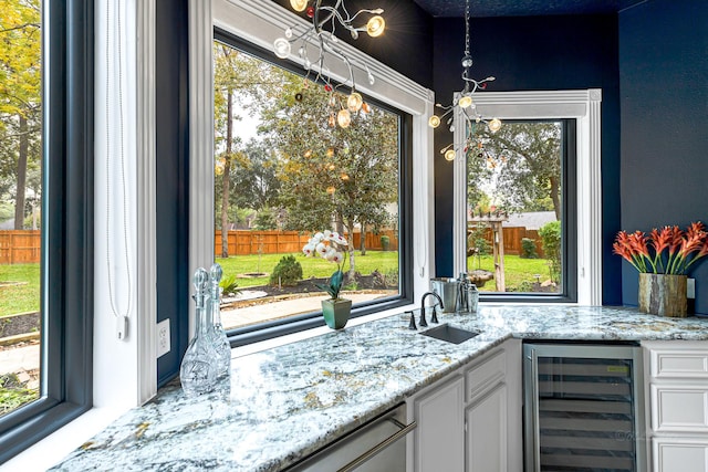 kitchen with light stone counters, beverage cooler, a sink, white cabinetry, and stainless steel dishwasher