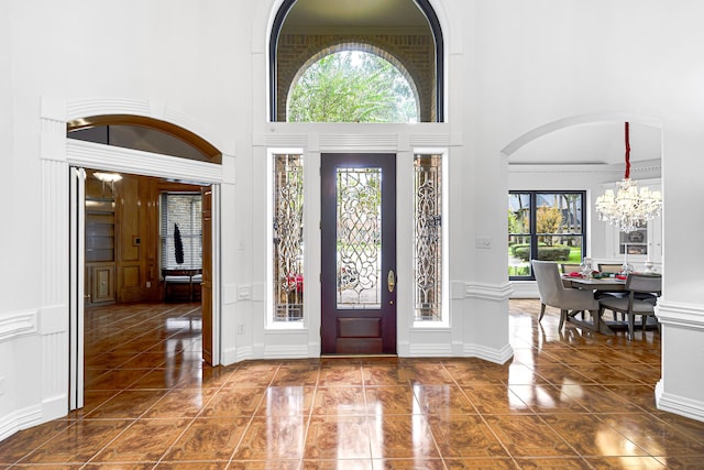 tiled foyer entrance featuring a notable chandelier, a decorative wall, and a high ceiling