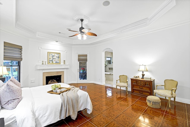 tiled bedroom featuring baseboards, a tray ceiling, ornamental molding, a fireplace, and arched walkways