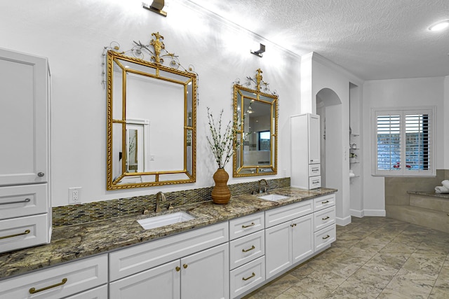 full bath with a textured ceiling, double vanity, crown molding, and a sink