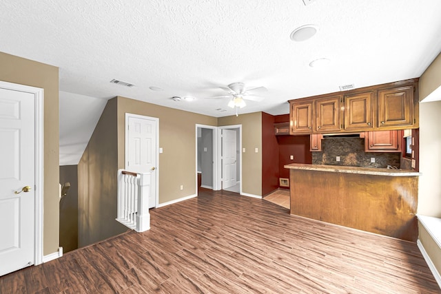 kitchen featuring wood finished floors, visible vents, a peninsula, decorative backsplash, and light countertops