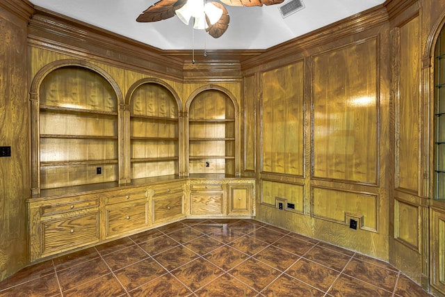 interior space featuring wooden walls, built in shelves, a ceiling fan, visible vents, and dark tile patterned flooring