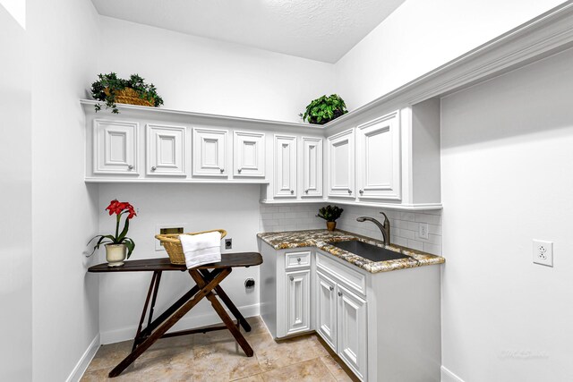 clothes washing area featuring baseboards, hookup for an electric dryer, cabinet space, a sink, and washer hookup