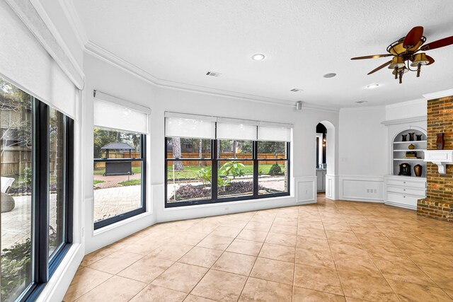 unfurnished living room featuring tile patterned flooring, visible vents, a wainscoted wall, ornamental molding, and arched walkways