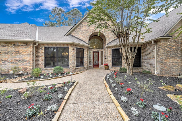 property entrance featuring brick siding and a shingled roof