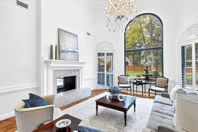 living area with visible vents, a tiled fireplace, wood finished floors, a high ceiling, and an inviting chandelier