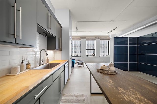 kitchen featuring gray cabinetry, butcher block counters, dishwasher, decorative backsplash, and a sink