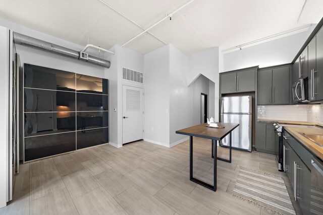 kitchen featuring visible vents, backsplash, a high ceiling, appliances with stainless steel finishes, and baseboards