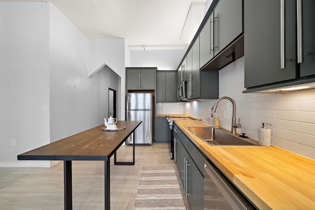 kitchen featuring a sink, stainless steel appliances, rail lighting, wood counters, and tasteful backsplash