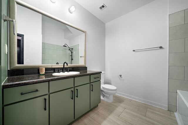 full bathroom featuring visible vents, baseboards, toilet, a tile shower, and vanity