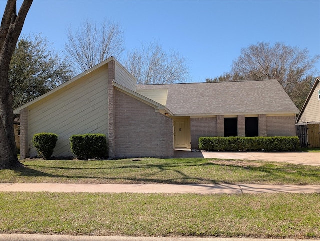 mid-century inspired home with brick siding, a front yard, and roof with shingles