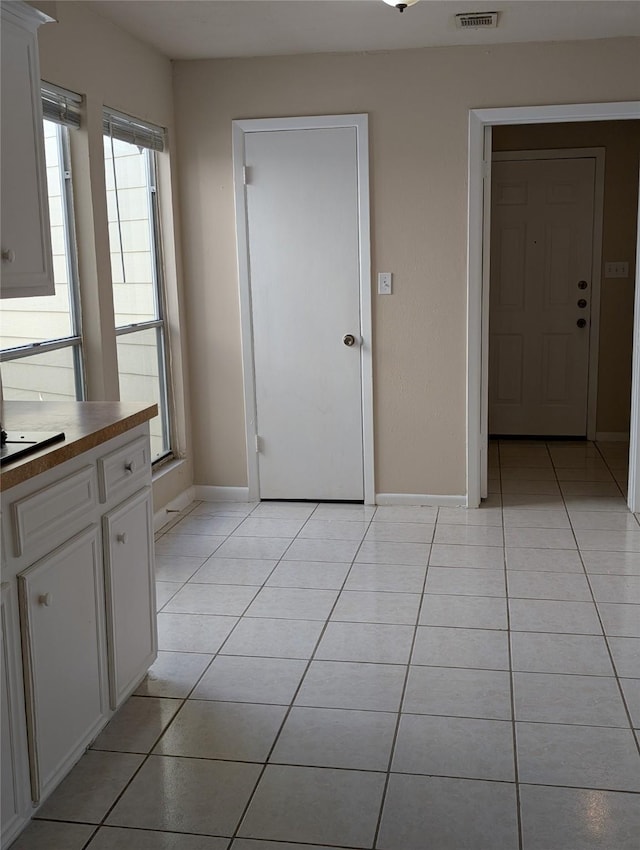 interior space featuring white cabinetry, light tile patterned floors, visible vents, and baseboards