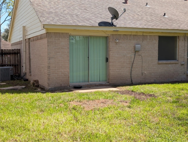 exterior space featuring brick siding, central AC unit, a shingled roof, and a yard