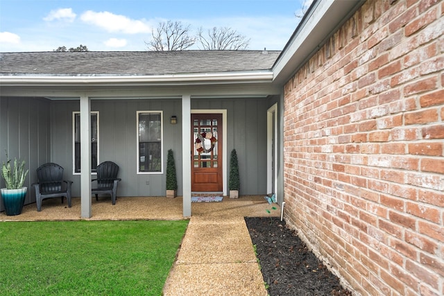 entrance to property featuring a yard, brick siding, and roof with shingles