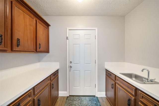 clothes washing area featuring a textured ceiling, wood finished floors, baseboards, and a sink