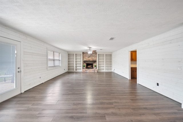 unfurnished living room featuring built in features, a fireplace, dark wood-style flooring, and a textured ceiling