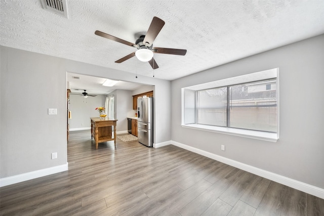 unfurnished living room with dark wood-style floors, visible vents, a textured ceiling, and baseboards