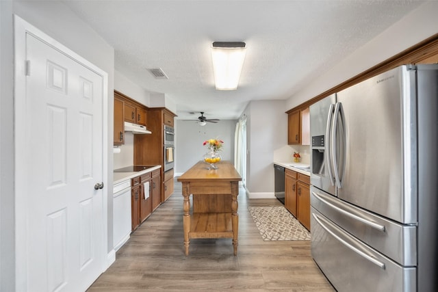 kitchen with visible vents, under cabinet range hood, light wood-type flooring, brown cabinetry, and black appliances