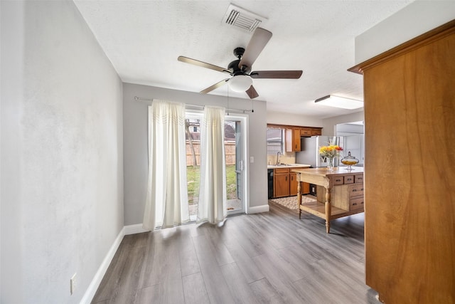 living area with light wood finished floors, visible vents, a textured ceiling, and baseboards